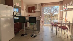 Cocina compacta con refrigerador, horno y comedor con sillas y mesa.