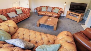 A living room with a brown leather sofa, a wooden coffee table, and a television on a wooden stand. - Hazelmere (Keswick)