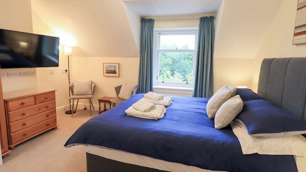 A bedroom with a large bed, a TV, a desk, and a window with curtains. - Hazelmere (Keswick)