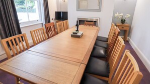 A dining area with a long wooden table, six wooden chairs, a television, a fireplace, and a small table with flowers. - Hazelmere (Keswick)