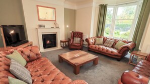 A living room with a fireplace, leather sofas, a wooden coffee table, and a television. - Hazelmere (Keswick)