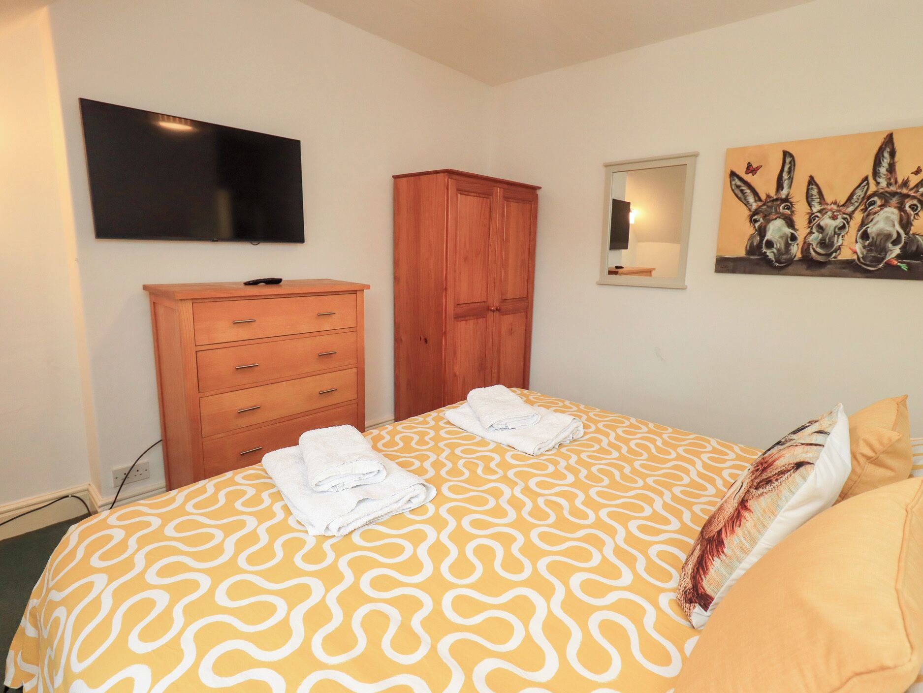 A hotel room with a bed, a wooden wardrobe, a flat-screen TV, and a painting of donkeys.