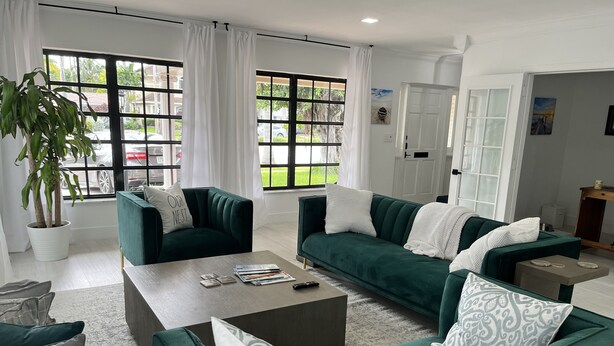 A modern living room with green sofas, a coffee table, and a large window with curtains. - Walk to the Beach and everything else (Hollywood)