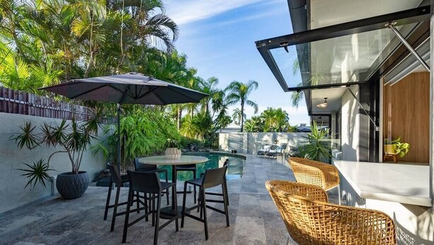An outdoor patio with a pool, surrounded by tropical plants and furnished with a table and chairs. - Sorrento Oasis - 5BR, Gym, Pool (Bundall)
