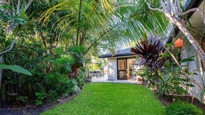A lush garden with a well-maintained lawn, a small building with a glass door, and various tropical plants. - Sorrento Oasis - 5BR, Gym, Pool (Bundall)