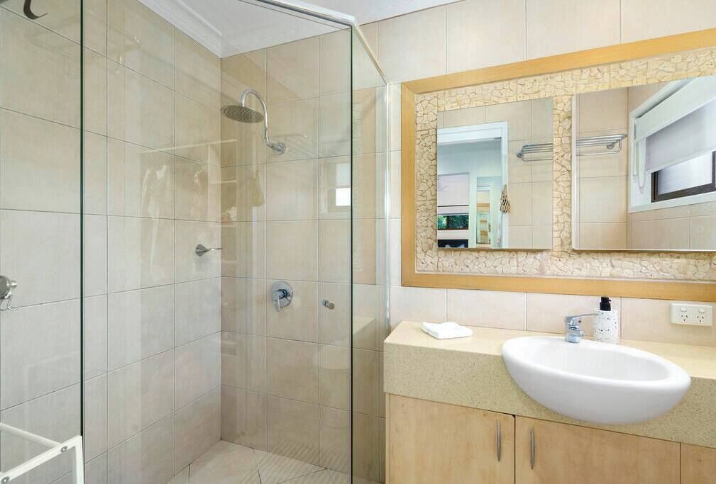 Een moderne badkamer met een douche in een glazen cabine, een witte wastafel en een grote spiegel met een stenen omlijsting.