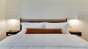 Una cama bien hecha con ropa de cama blanca y marrón, dos mesitas de noche con lámparas y un cabecero de madera.