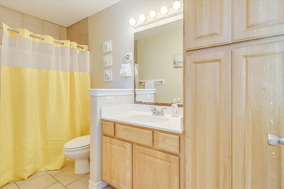 A bathroom with a white sink, wooden cabinets, a toilet, and a shower curtain.