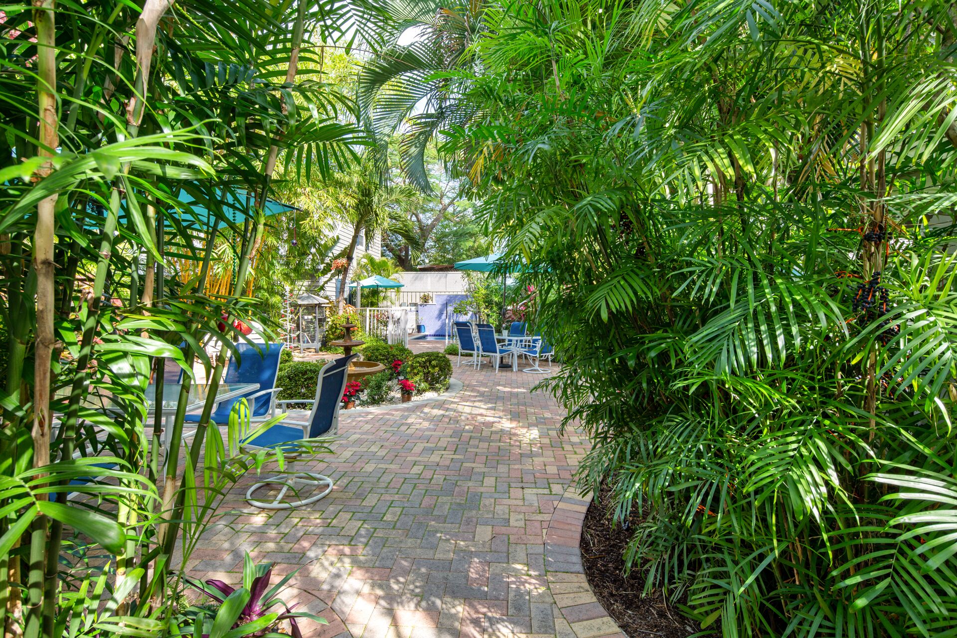 A paved garden path with a fountain, surrounded by lush greenery and outdoor seating.