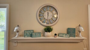 Un reloj de pared con diseño playero, una estantería con adornos y una pequeña planta en maceta.