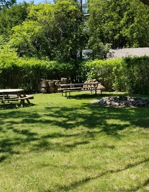 Relax in a serene outdoor setting surrounded by lush greenery and mature trees, with two picnic tables for a peaceful retreat.