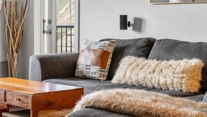 A grey sofa with patterned and fur throw pillows, a wooden coffee table, and a vase with dried reeds.