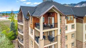 A multi-story building with balconies, a stone facade, and a view of mountains.