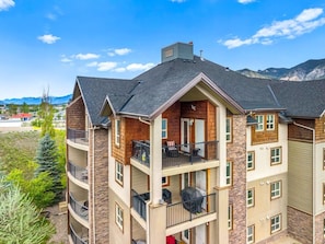 A multi-story building with balconies, a stone facade, and a view of mountains.