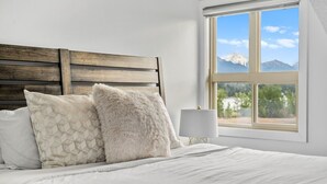 A bed with a wooden headboard, two pillows, a bedside lamp, and a window with a mountain view.