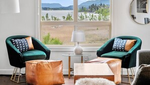 A room with two green armchairs, a small table, a lamp, and a view of a lake and mountains.