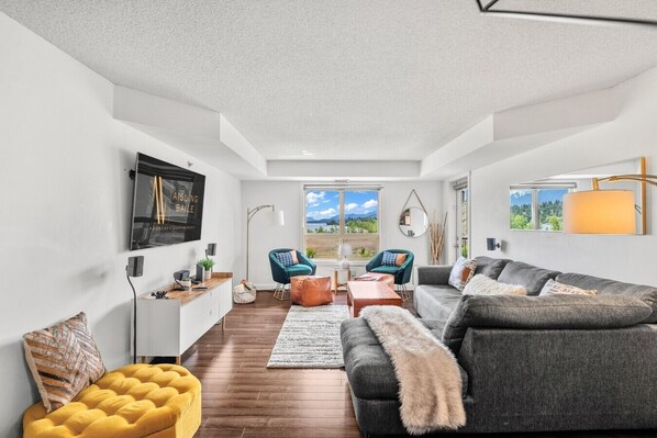 Un salon moderne avec un canapé, des fauteuils, une table basse et un téléviseur fixé au mur.