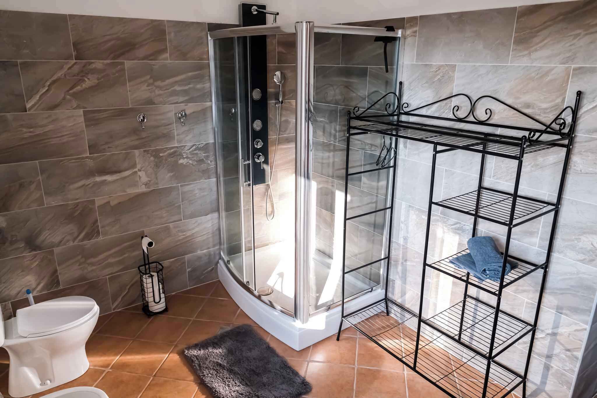 Un baño con ducha envuelta en vidrio, inodoro blanco y estantería metálica.
