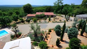 Um terreno ajardinado com piscina, um edifício de pedra e diversas árvores e arbustos.