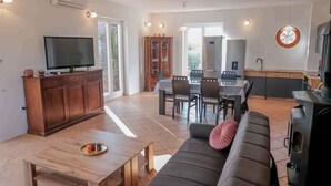 Uma sala de estar moderna com televisão de tela plana, móveis de madeira, um espaço de refeições com mesa e cadeiras e uma cozinha com fogão e pia.