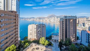 Un paysage urbain côtier avec de hauts immeubles, une marina et un ciel bleu dégagé.