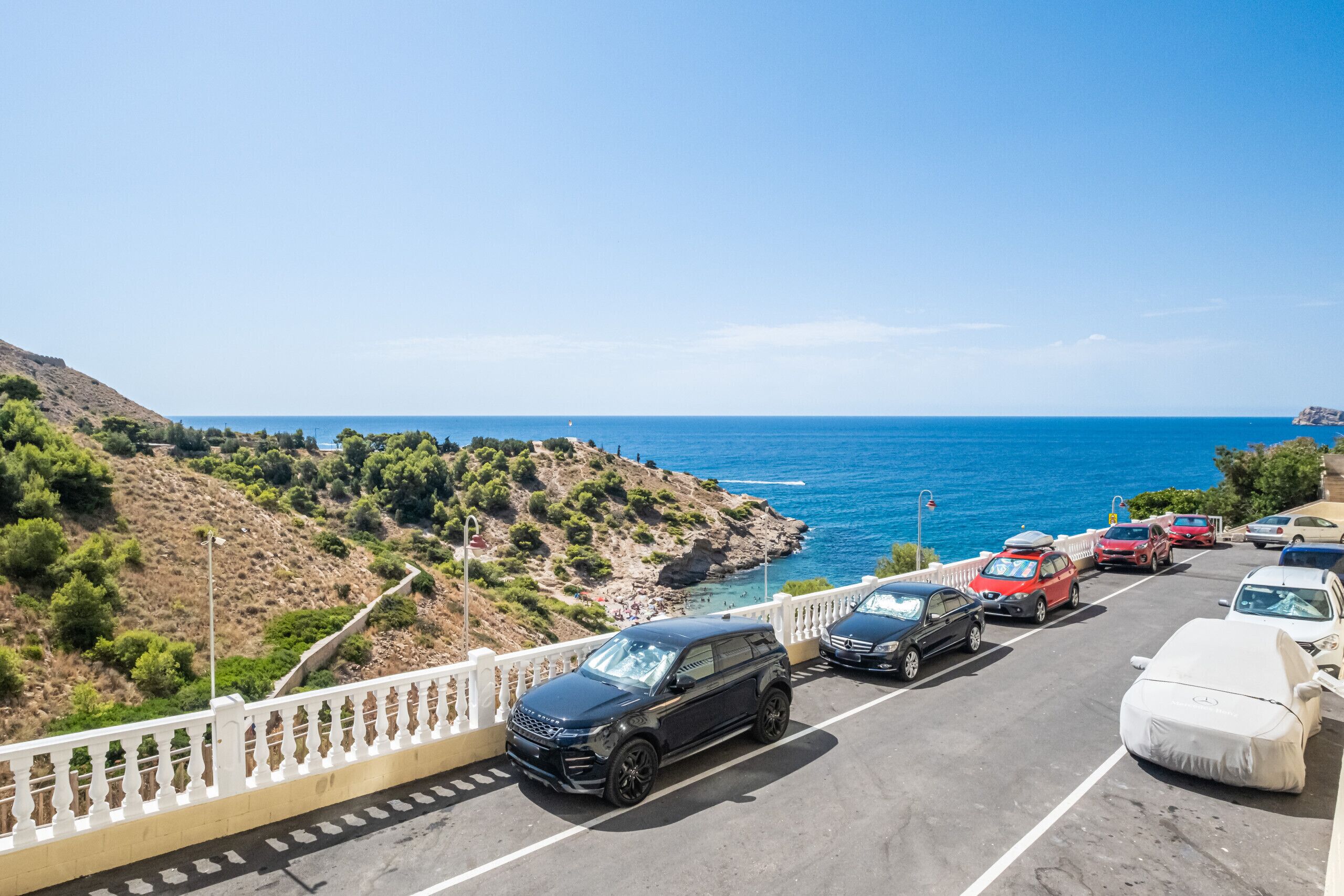 A parking area with cars and a white fence overlooking a coastal landscape.