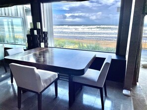 A modern dining area with a large table and chairs, a view of the ocean through large windows, and a glass partition.
