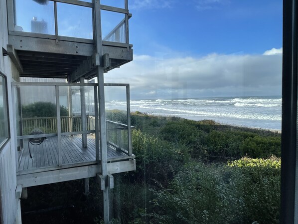 A wooden observation tower with a glass enclosure, overlooking a beach with waves and dense vegetation.