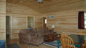 A wooden cabin interior with a sofa, dining table, chairs, and a ceiling fan. - Cottage 1 on Beautiful Fox Lake! (Fox Lake)