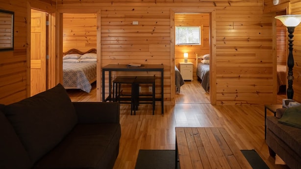 A cozy cabin interior with a wooden floor, a sofa, a dining table with chairs, a bed with a canopy, and a lamp. - Cottage 1 on Beautiful Fox Lake! (Fox Lake)