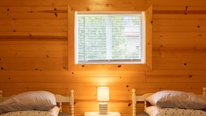 A cozy cabin room with two beds, a small bedside table with a lamp, and a window with blinds. - Cottage 1 on Beautiful Fox Lake! (Fox Lake)