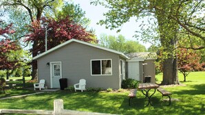 A small, single-story house with a front porch, a covered patio, and a fenced yard. - Cottage 1 on Beautiful Fox Lake! (Fox Lake)