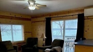 A cozy cabin interior with a wooden floor, a ceiling fan, a sofa, a chair, and a dining table.