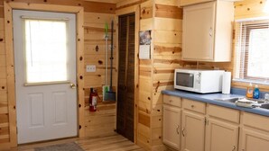 A wooden cabin interior with a white door, a microwave on the counter, and a fire extinguisher on the wall.