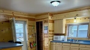 A wooden interior with a kitchen area, including cabinets, a microwave, and a dining table.