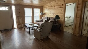 Ett mysigt rum med ett träpanelat tak, en soffa, en fåtölj, ett litet bord och en lampa.