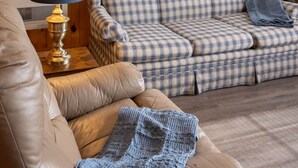 Ein gemütliches Wohnzimmer mit einem karierten Sofa, einem Ledersessel und einer Strickdecke.