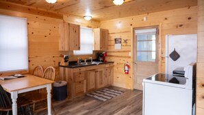Puinen mökki, jonka sisätiloissa on keittiö, ruokailutila ja pieni jääkaappi.