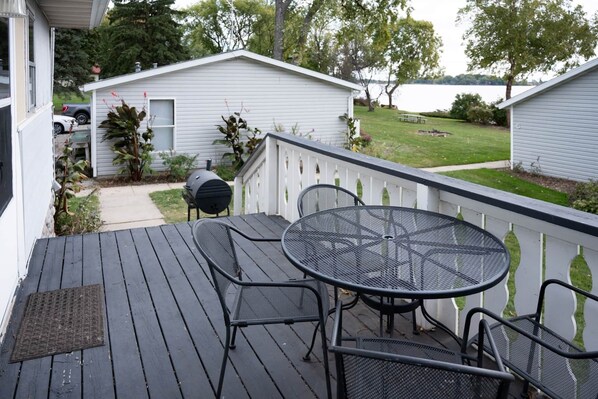 A deck with a round table and chairs, a barbecue grill, and a small shed in the background.