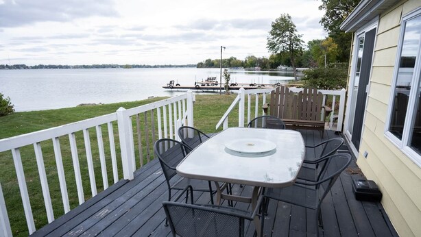 Eine Terrasse mit Tisch und Stühlen mit Blick auf einen See, mit einem weißen Zaun und einem Steg mit Booten im Hintergrund.