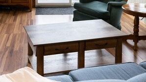 Ein Wohnzimmer mit einem Holztisch, einem grünen Sessel, einer Couch, einem Fernseher und Blick auf eine Terrasse und Wasser.