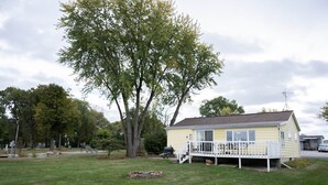 Ein eingeschossiges, gelbes Haus mit einer Terrasse und einem großen Baum davor.