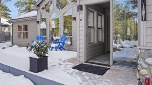 Une maison dotée d’un porche abrité, d’une porte-fenêtre coulissante et d’un petit jardin agrémenté d’un pot de fleurs et de chaises bleues.