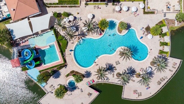 Vista aerea di un resort con una grande piscina centrale, uno scivolo d'acqua e palme.