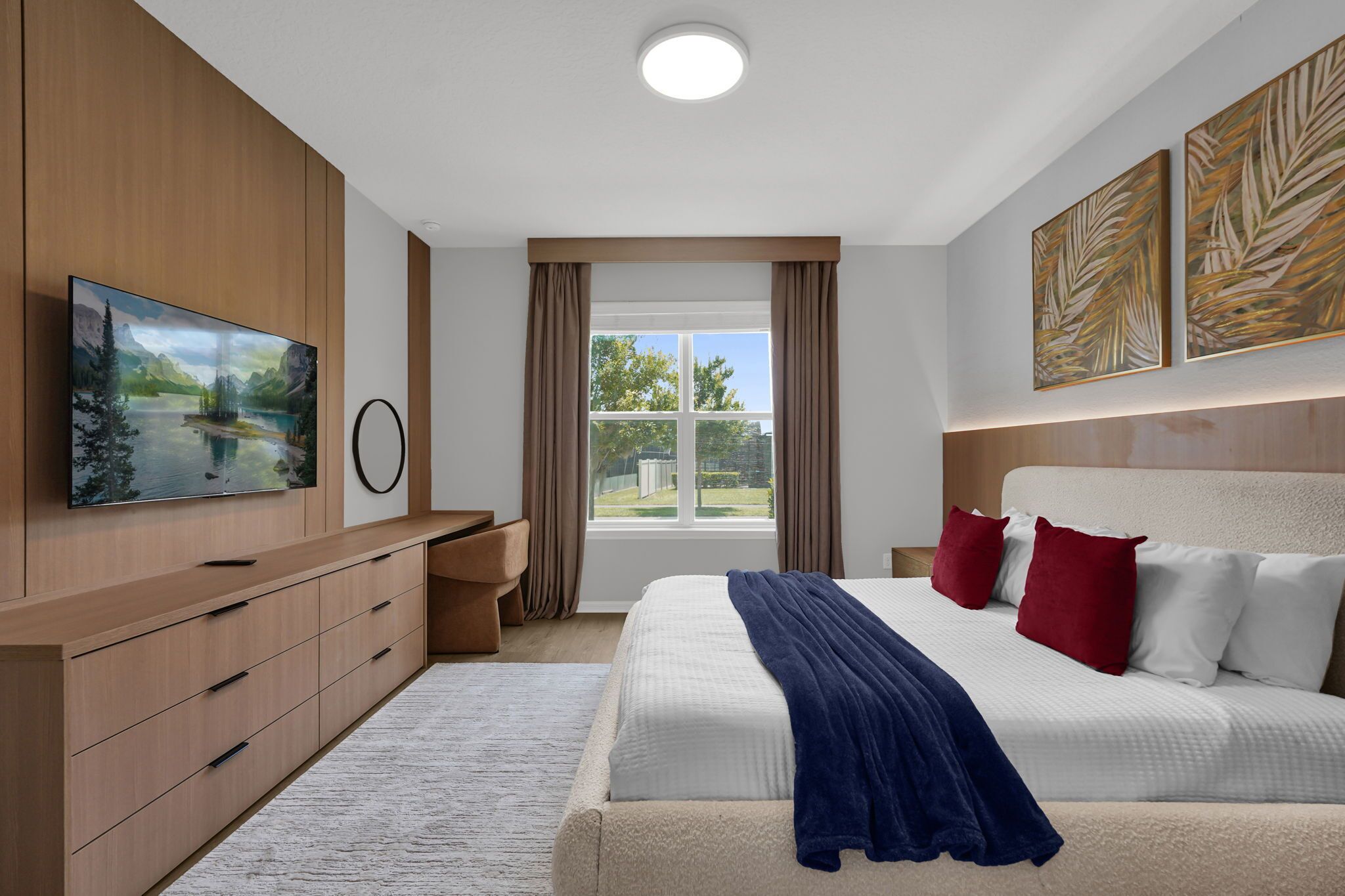 Ein Schlafzimmer mit einem großen Bett, einem an der Wand befestigten Fernseher, einem Fenster mit Vorhängen und Wandbildern.