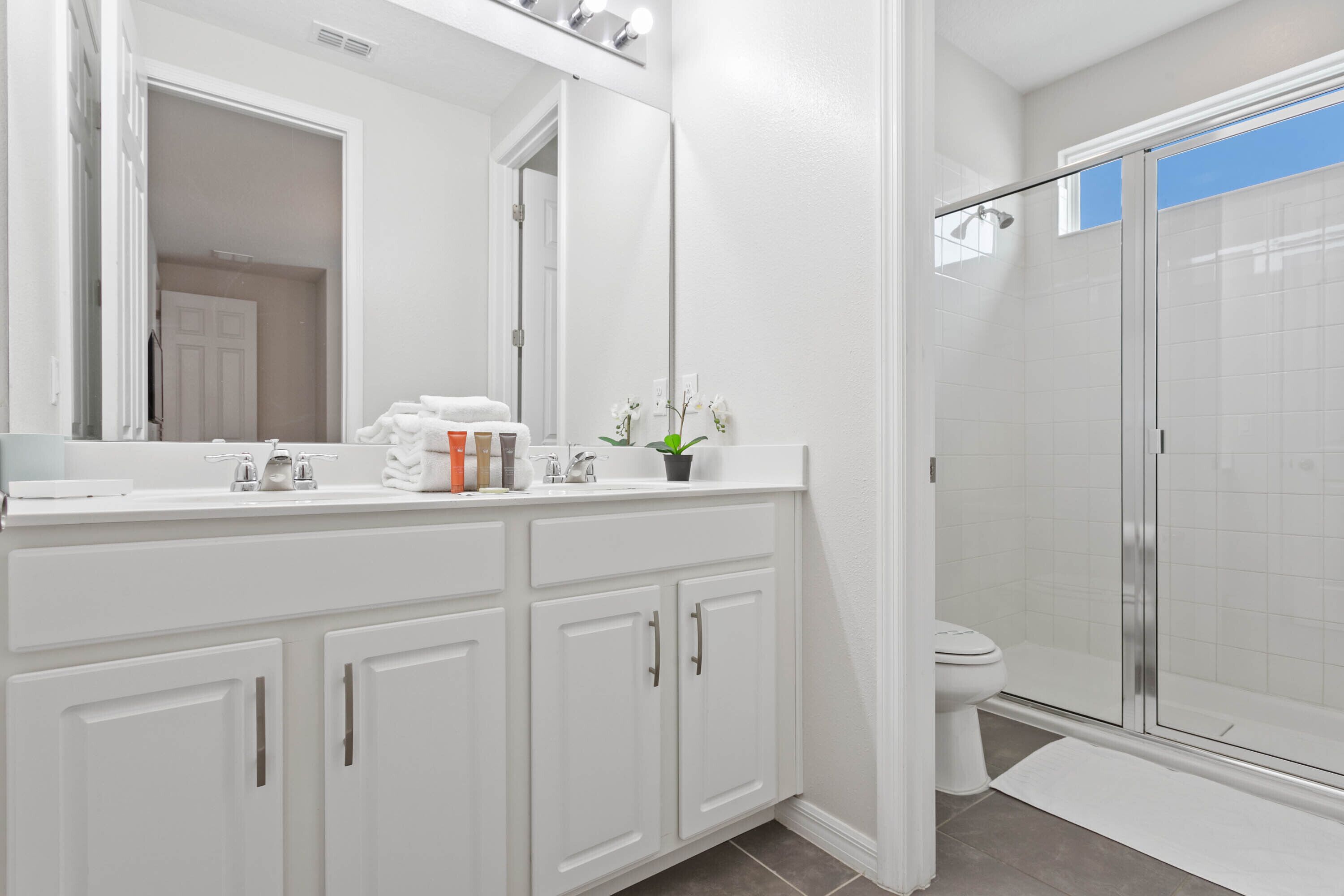 A modern bathroom with white cabinetry, a large mirror, a shower with glass doors, and a toilet.