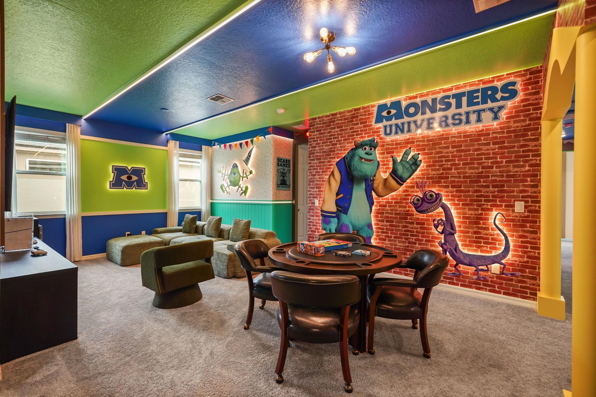 A room with a Monsters University mural, a round table with chairs, and a couch.