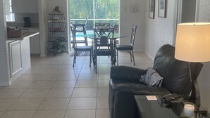 Een ruime woonkamer met een eettafel en stoelen, een zwarte leren bank en een glazen salontafel.