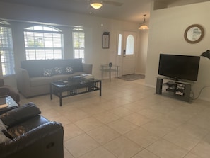 A living room with a sofa, coffee table, TV, and a glass table.