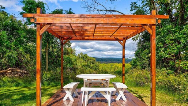 Eine Holz-Pergola mit Picknicktisch und Bänken in einem üppigen Garten.